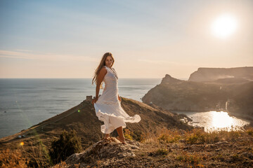 A woman in a white dress stands on a hill overlooking the ocean. The scene is serene and peaceful, with the woman's dress billowing in the wind. The combination of the ocean.