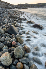 Round stones on the beach with waves crashing to the shore on a summer evening. Sør-Varanger, Finnmark, Northern Norway