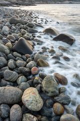 Round stones on the beach with waves crashing to the shore on a summer evening. Sør-Varanger, Finnmark, Northern Norway