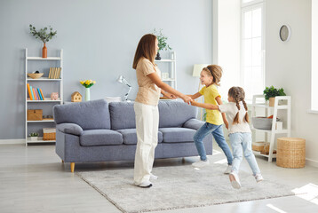 Obraz premium Playful funny dance of active family, mother parent, babysitter, cute small children daughter, son dancing together in living room interior, carefree little kids fun laughing enjoy leisure home