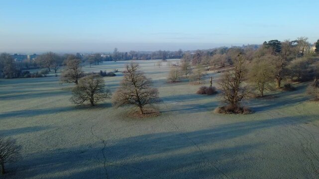 View from a drone flying forwards over Prospect Park in Reading, Berkshire, UK in the winter. It is early morning and the landscape is coloured white by a sharp frost