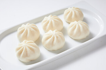 Steamed bao buns in a white rectangular plate on a white plain background.