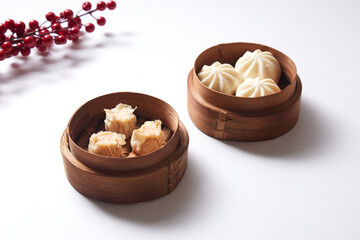 Steamed bao buns and dimsum in a traditional bamboo steamer on a white plain background.