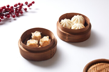 Steamed bao buns and dimsum in a traditional bamboo steamer on a white plain background.