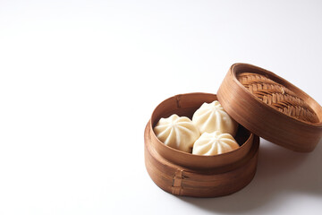 Steamed bao buns in a traditional bamboo steamer on a white plain background.