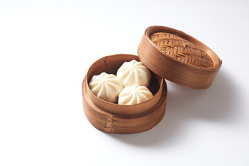 Steamed bao buns in a traditional bamboo steamer on a white plain background.