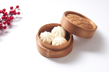 Steamed bao buns in a traditional bamboo steamer on a white plain background.