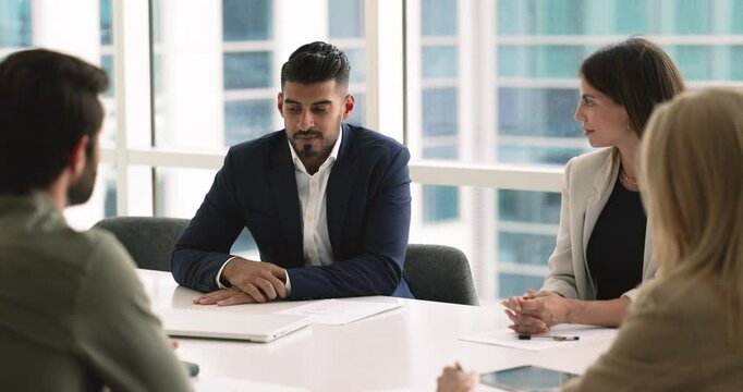 Successful young Indian business leader man talking to partners at meeting, sitting at table, speaking. Company executive, CEO discussing project financial strategy with colleagues, investors