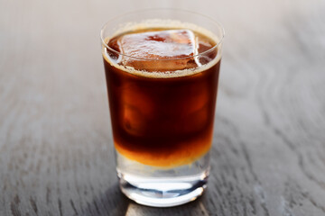 Espresso tonic with clear ice cube in tumbler glass on oak wood table with copy space