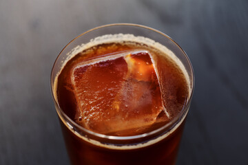 Closeup espresso tonic with clear ice cube in tumbler glass on oak wood table