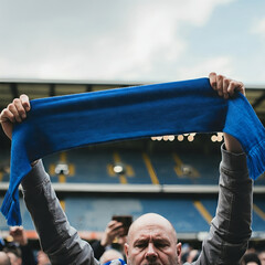 The hands of football supporters raise a plain blue scarf to the sky in the stadium stands