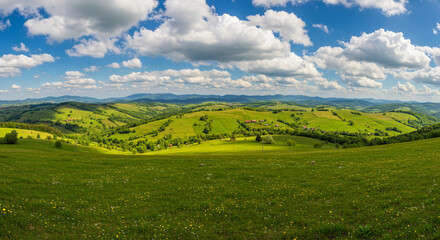 Obraz premium A picturesque landscape showcasing a lush green meadow with a charming village nestled amidst rolling hills under a bright, sunny sky, with an idyllic landscape