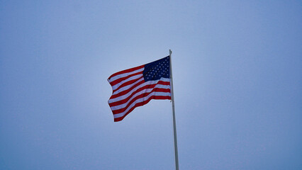 U.S. flag waving against a clear blue sky during a sunny day in a public park