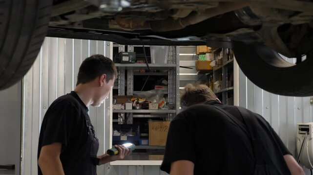 Two car mechanics working under the car on a lift in the garage. Car underbody repair in a modern car repair shop.