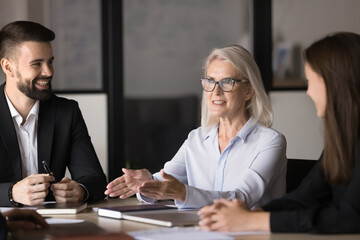 Group of entrepreneurs gathered together at meeting led by smiling middle-aged businesslady...