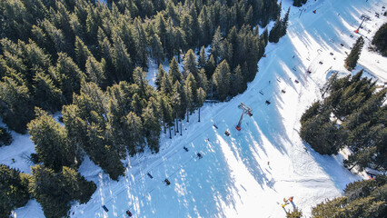 Drone view of a ski slope from above, showcasing skiers on the trail and a chairlift transporting...