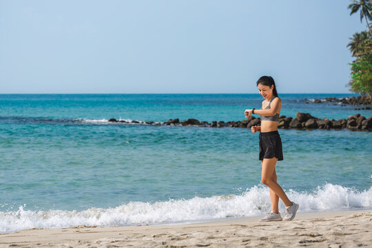 Sport healthy wellness fitness technology vacation concept of Young happy asian runner fit woman using smart watch and run on the beach Thailand