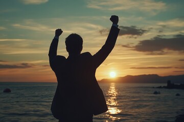 Silhouetted businessman celebrating success at sunset by the sea a symbol of achievement