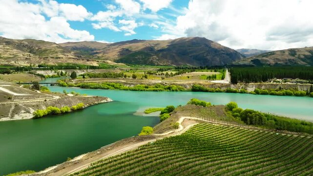 Aerial Scenic View Of Tranquil River By Mountains, Drone Flying Forward Over Green Field On Sunny Day - Bannockburn, New Zealand