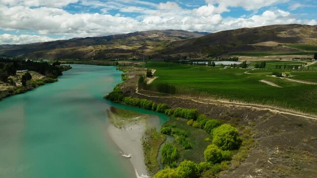 Aerial Panning Shot Of River Flowing Amidst Green Mountains Under Clouds In Sky - Bannockburn, New Zealand