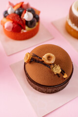 Chocolate tart covered with chocolate velour and topping with sliced nuts on pink background.	