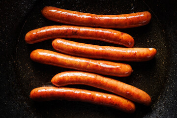 Fried pork and lamb sausages on a dark background in a frying pan, top view
