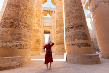 Woman traveler explores the ruins of the ancient Karnak temple in the city of Luxor in Egypt. Great row of columns with carved hieroglyph