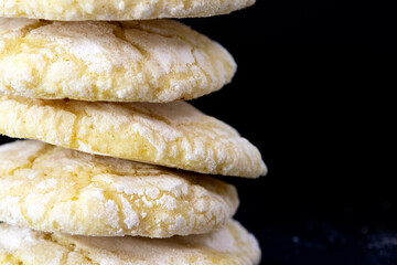 Close-up of round flat cracked cookies arranged in a pyramid, sprinkled with powdered sugar on a black background.