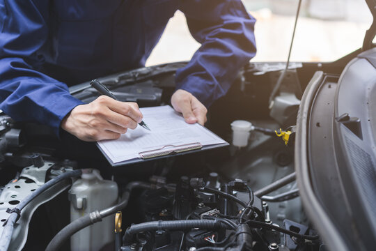 Auto check, car service shop concept. Automobile repairman writing job checklist on clipboard, mechanic checking engine to estimate repair machine, inspecting maintenance by engineer at vehicle garage