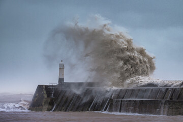 A huge winter storm hitting the coast of the UK. Giant waves crash into a breakwater, with a...