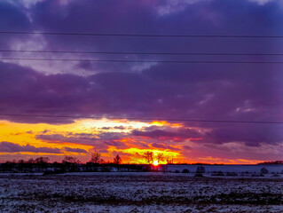 A sunset over a snowy field with power lines in the foreground