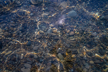 Underwater pebble backgrounds. Colorful stones sea bottom in the sun rays. View from above through clear water. Seascape wallpaper texture. Defocus.