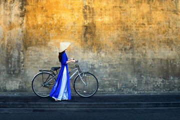 Vietnamese woman in traditional Vietnamese costume with old bicycle walks along the walls of a...
