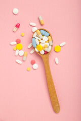 Assorted pharmaceutical medicine pills, tablets and capsules on wooden spoon on pink background. Vertical photo