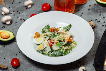Traditional caesar salad in a white bowl on a old white table with leaves and a sauce boat and parmesan. Selected focus.