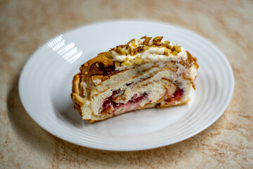 A single slice of a homemade meringue roll served on a white plate, showcasing its layers of fluffy meringue, creamy filling, and fresh berries. Captured in soft natural light