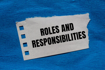 Roles and responsibilities message written on ripped torn paper piece with blue background....