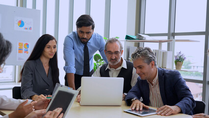group of diverse business people working together looking laptop computer discussing on table in meeting room . senior manager caucasian indian