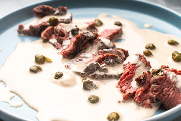 Thin slices of beef in vitello tonnato sauce. A traditional Italian dish of meat with tuna and anchovy cream sauce. close-up. High quality photo