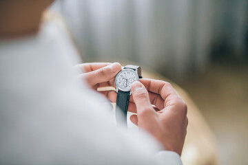 A person is holding a watch in their hand. The watch is silver and black. The person is wearing a...