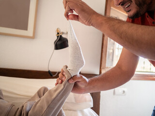 Man pulls on a sock of his child to remove it. Natural light filters through a nearby window,...
