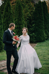 A bride and groom are walking down a path in a garden. The bride is wearing a white dress and holding a bouquet of flowers. The groom is wearing a suit and tie. The scene is romantic and happy