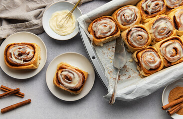 Freshly baked cinnamon rolls with cream cheese frosting and cinnamon sticks