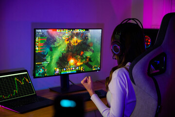 Asian gamer playing online video game excited on desktop computer PC display neon LED lights, woman...