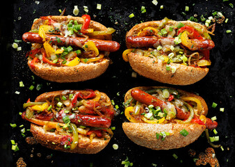 Sausage sandwiches with addition bell peppers and onion on a black background.  Hot dog form with added vegetables