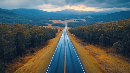 Scenic aerial view of a wet highway winding through a forest and mountain landscape during sunset.