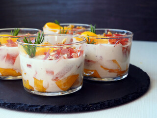 Individual Appetizer Glass with Creamy Mousse, Serrano Ham, Fresh Peach Slices, and Cheese Garnished with Rosemary
