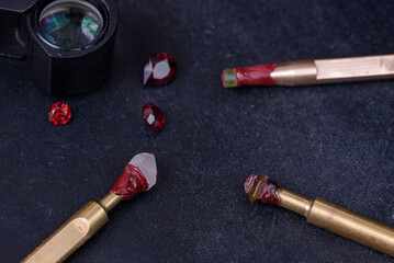 Lapidary craftsman bench with metal dops with faceted amethyst and peridot gemstones and rad garnet stones with a magnifying glass on the background.