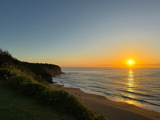 Fototapeta premium View of the sun rising over a beach and the headland in Australia 