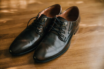 Two brown shoes with a brown lace on the front. The shoes are on a wooden table. The shoes are well-polished and look like they are ready to be worn